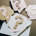 Artistic paper question marks on an open notebook with a pen, symbolizing curiosity and creativity.
